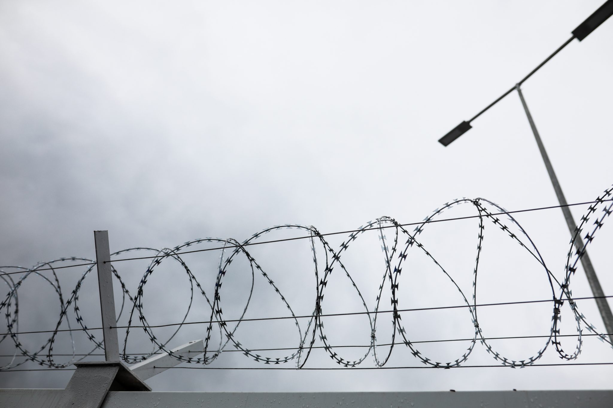 Shallow depth of field (selective focus) and filtered image with a razor wire on the outside wall of a governmental institution on a cloudy day.